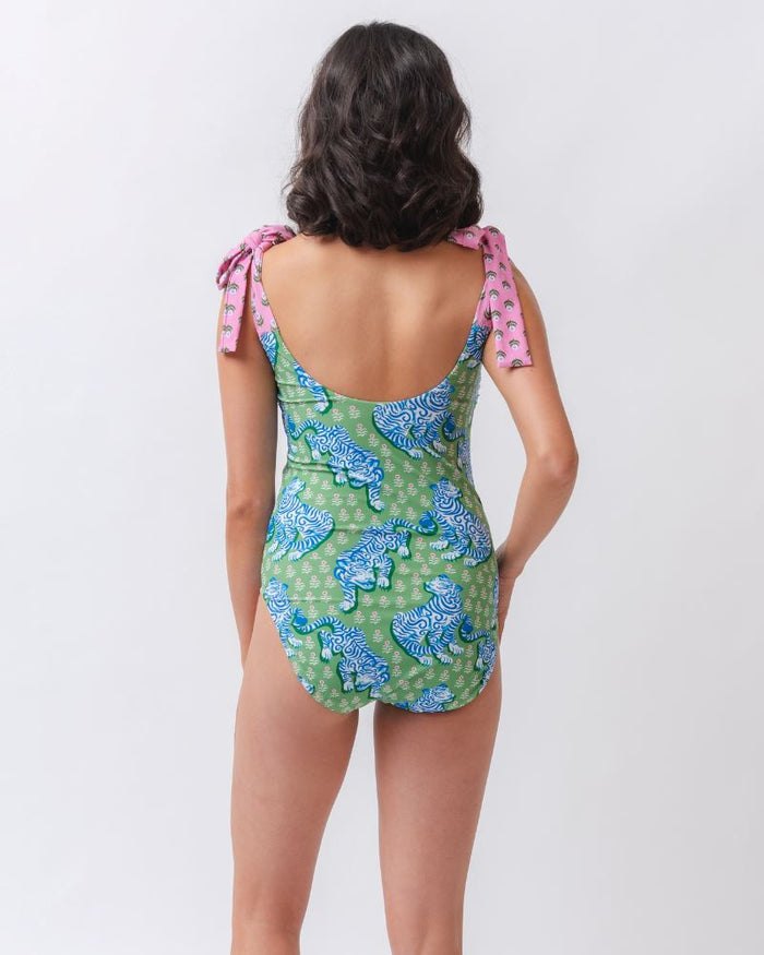 Photo of a woman with her back facing us wearing a bold green and pink tiger print shoulder tie swim one piece