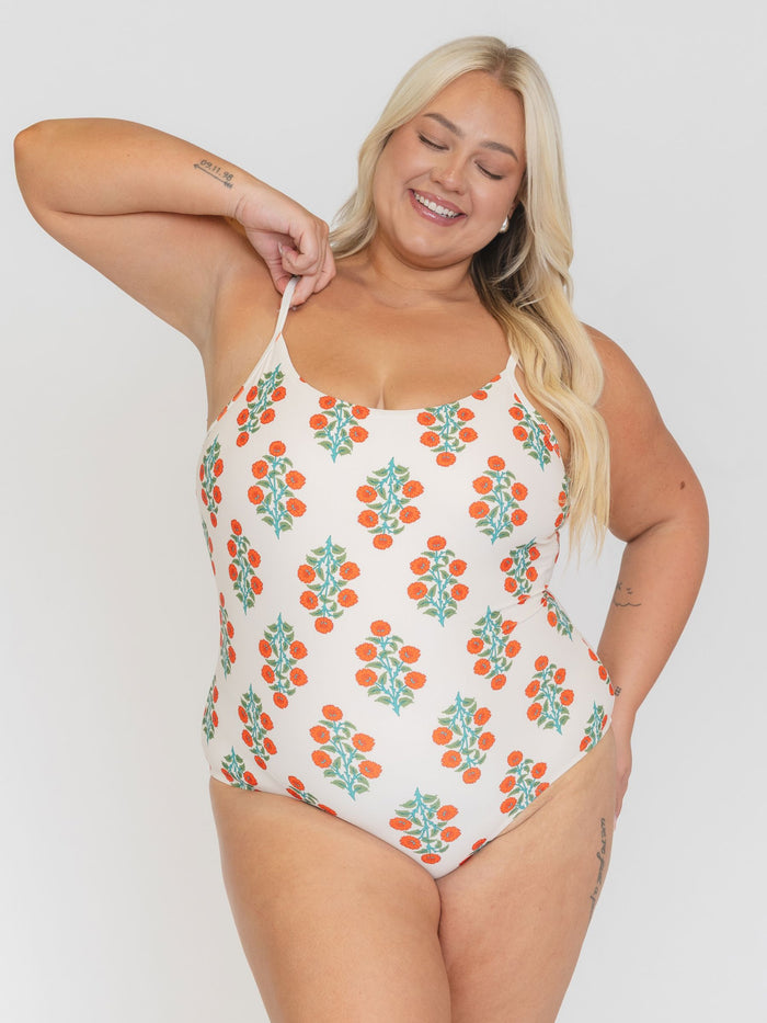 Woman wearing a white swimsuit with orange and green pattern on a plain background