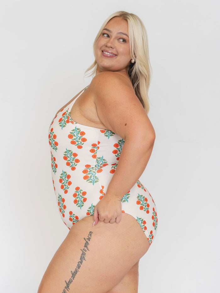 Side view of a woman wearing a white swimsuit with orange floral pattern on a plain background