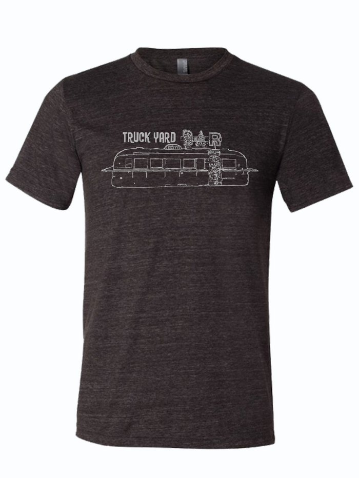 Dark, charcoal gray tshirt with graphic design of a metal trailer with a neon sign above it that reads "TRUCK YARD BAR."