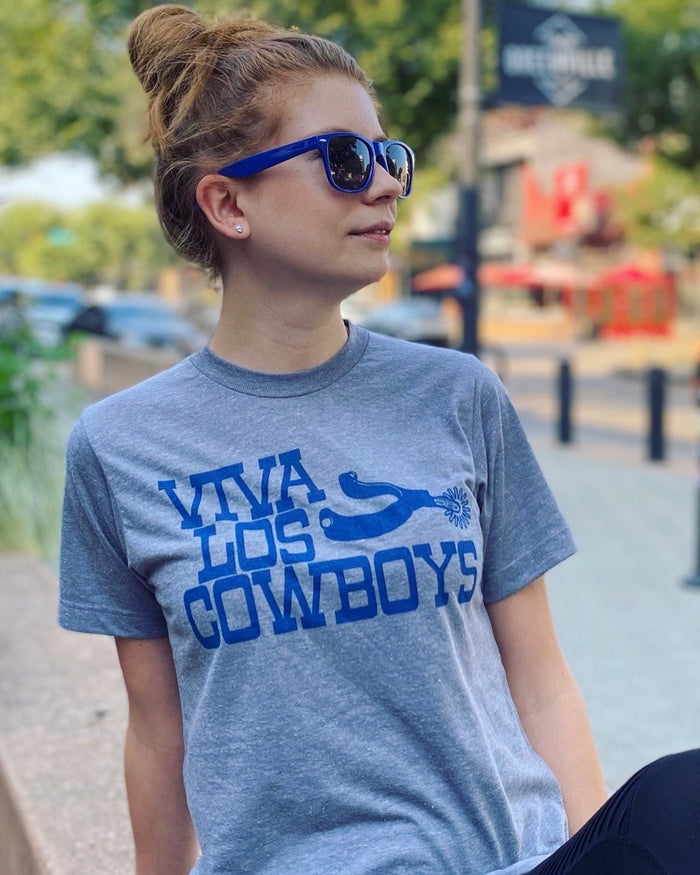Woman wearing a Bullzerk "Viva Los Cowboys" tshirt and blue sunglasses, sitting outdoors.