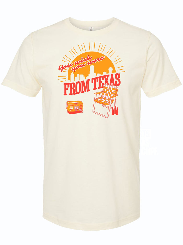 Cream tshirt with graphic design of a sunset over the Dallas skyline and text reading "You wish you were from Texas" above a folding chair and cooler with beer.